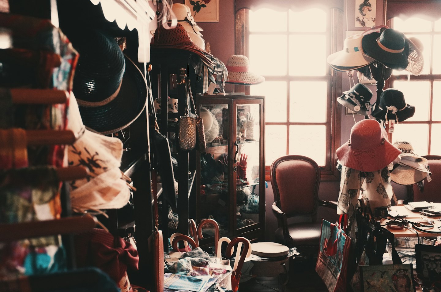 Various hats displayed in a vintage boutique with antique chairs.